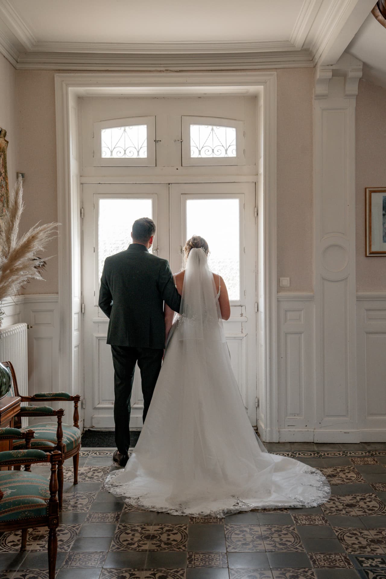 Les mariés de dos devant une grande porte-fenêtre du château