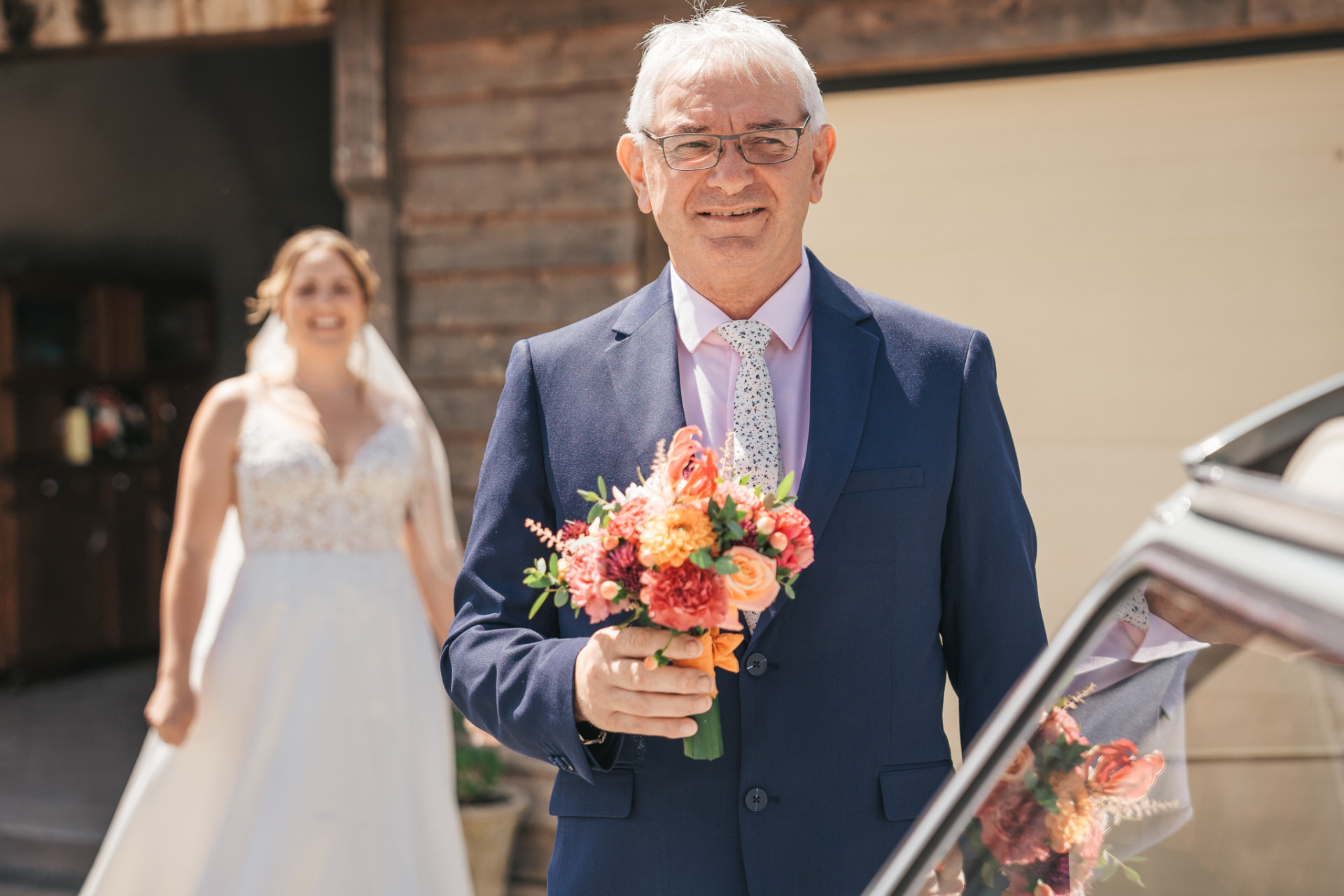 Le père de la mariée tenant le bouquet devant la voiture