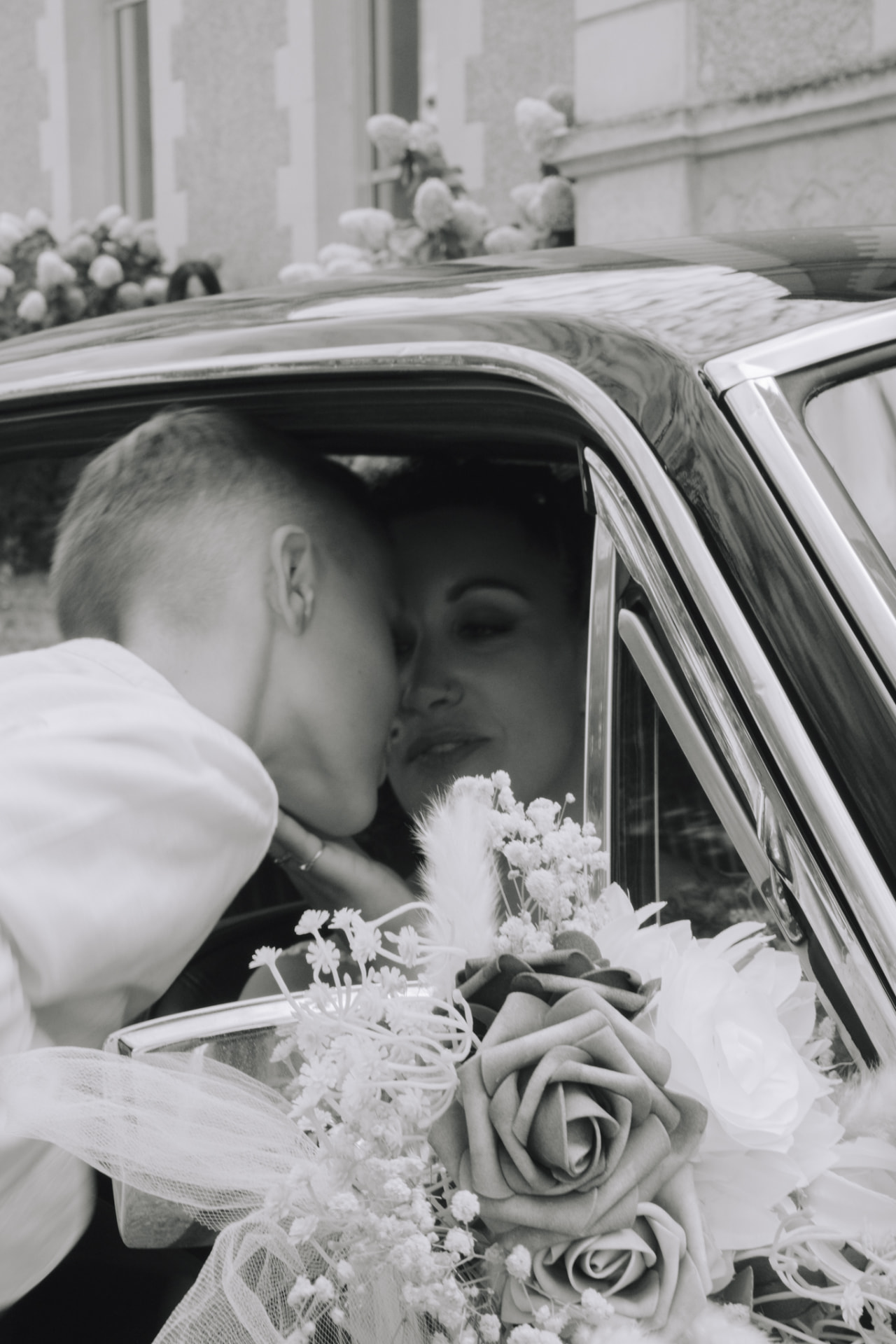 Un jeune garçon embrasse la mariée dans la voiture fleurie, en noir et blanc