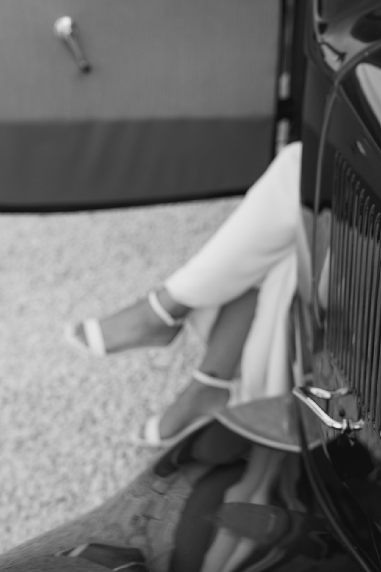 Détail des jambes de la mariée près d'une voiture ancienne, en noir et blanc